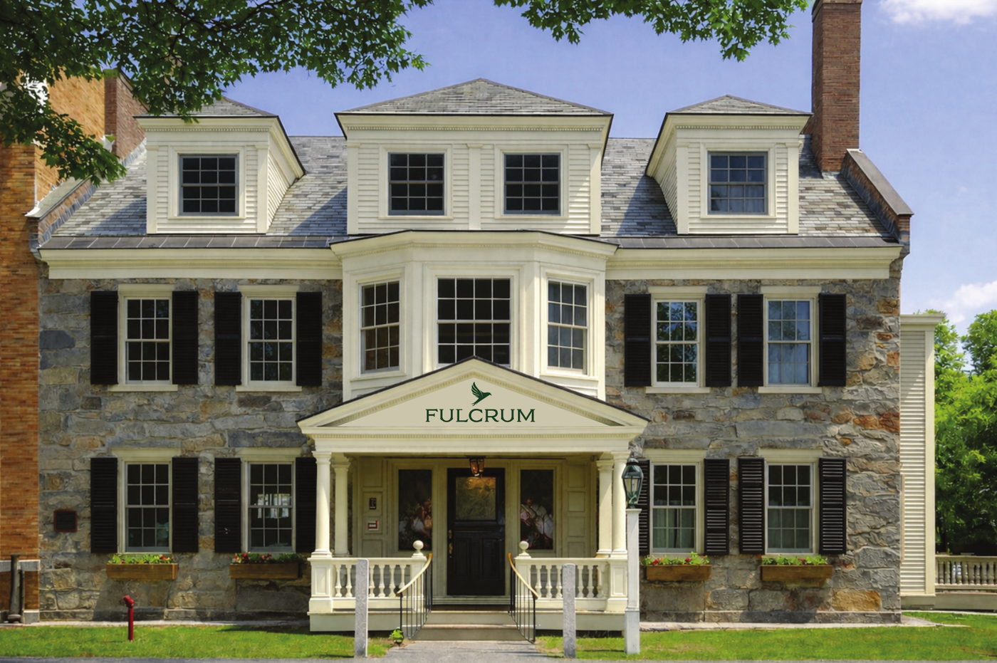 Fulcrum House, a three-storey stone and clapboard building at 4 The Green, Woodstock, Vermont, with a white columned entrance porch and black shutters.